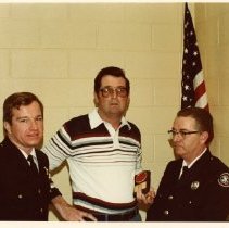 Two Fire Fighters and a man holding a plaque