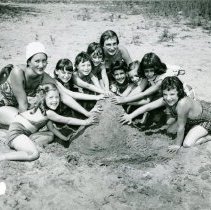 Group of girls with counselors making sand pile on beach at Camp Ideal