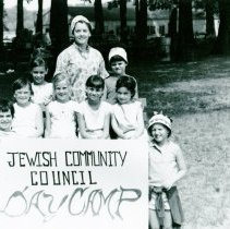 Counselor with children holding a "Jewish Community Council Day Camp" sign