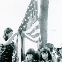 Barbara Natkow raising flag with children who have their right hands over t