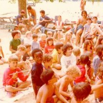 Color photo of boys and counselors sitting on beach and at picnic tables