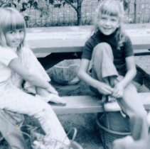 Two girls smiling while sitting at picnic table; one is tying her shoe
