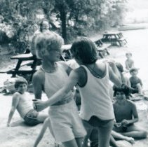 Two children dancing together in front of other children on beach