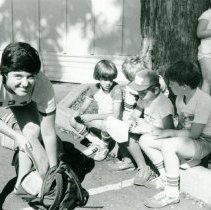 Campers sitting on curb with counselor in foreground