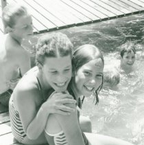 Two girls sitting together and smiling on pier with other children in backg