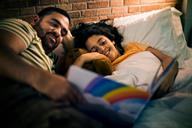 A parent reading a book with a child in bed.