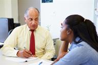Seated adult talking to a seated teenager. Adult is writing on paper.
