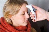 A person holding a forehead thermometer to another person's head.