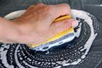 A person's hand cleaning a counter with a soapy sponge.
