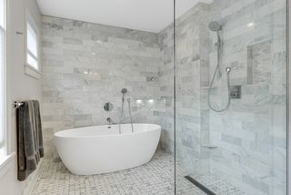 Large soaker tub opens to curbless shower area with marble walls and floors