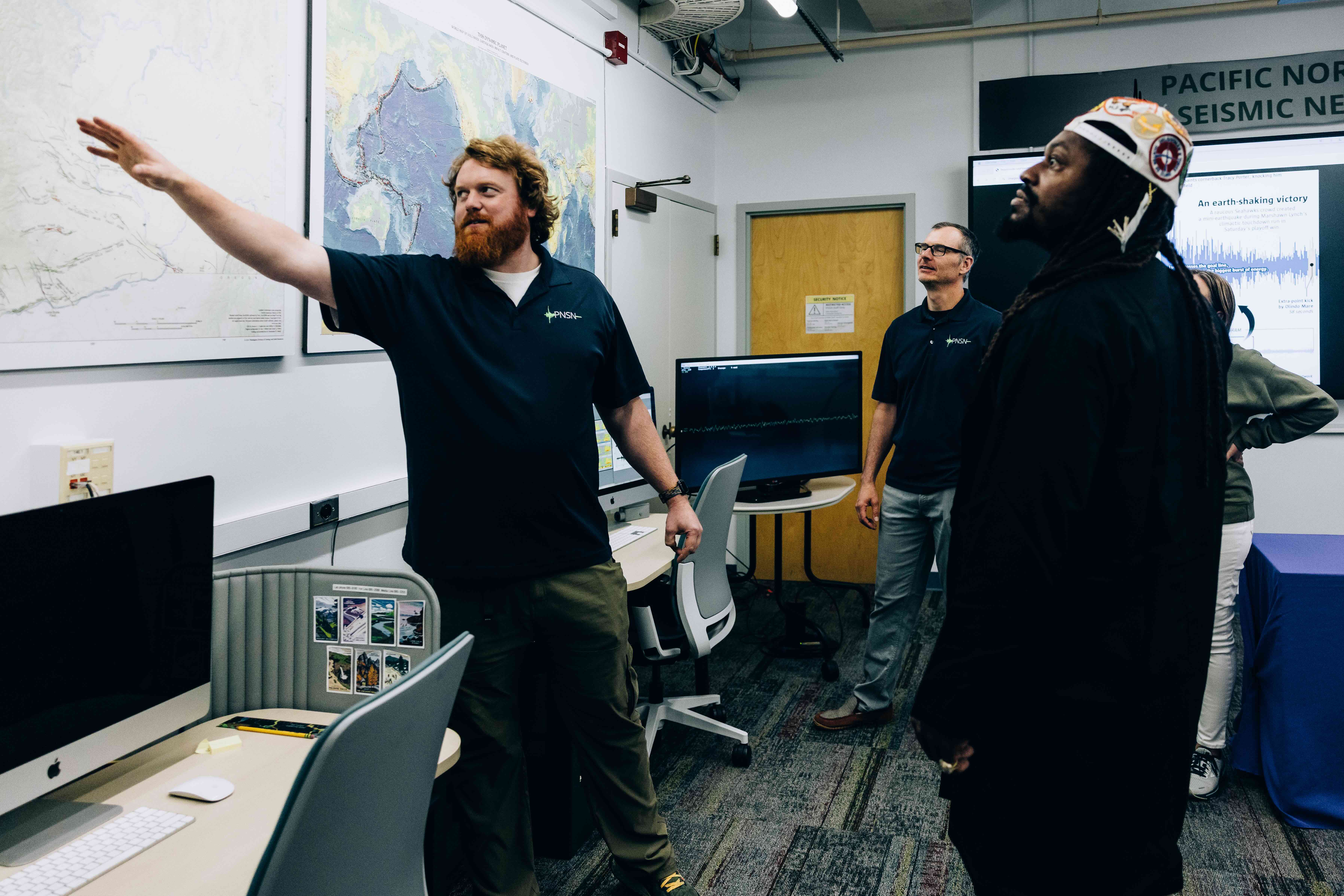 Pacific Northwest Seismic Network staffer Doug Gibbons showing former Seahawks player Marshawn Lynch a map of earthquakes in Washington State.  Staffer Alex Hutko stands in the background.