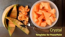  Presentation with shot - Colorful presentation theme enhanced with high angle shot of a bowl full of cantaloupe pieces next to the rinds and seeds a knife and spoon are also on the metal kitchen surface backdrop and a tawny brown colored foreground