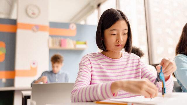 Student works on a math task in a classroom as classmates work nearby.