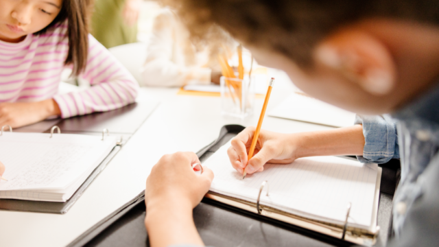 Two elementary students write in notebooks during a hands-on math activity