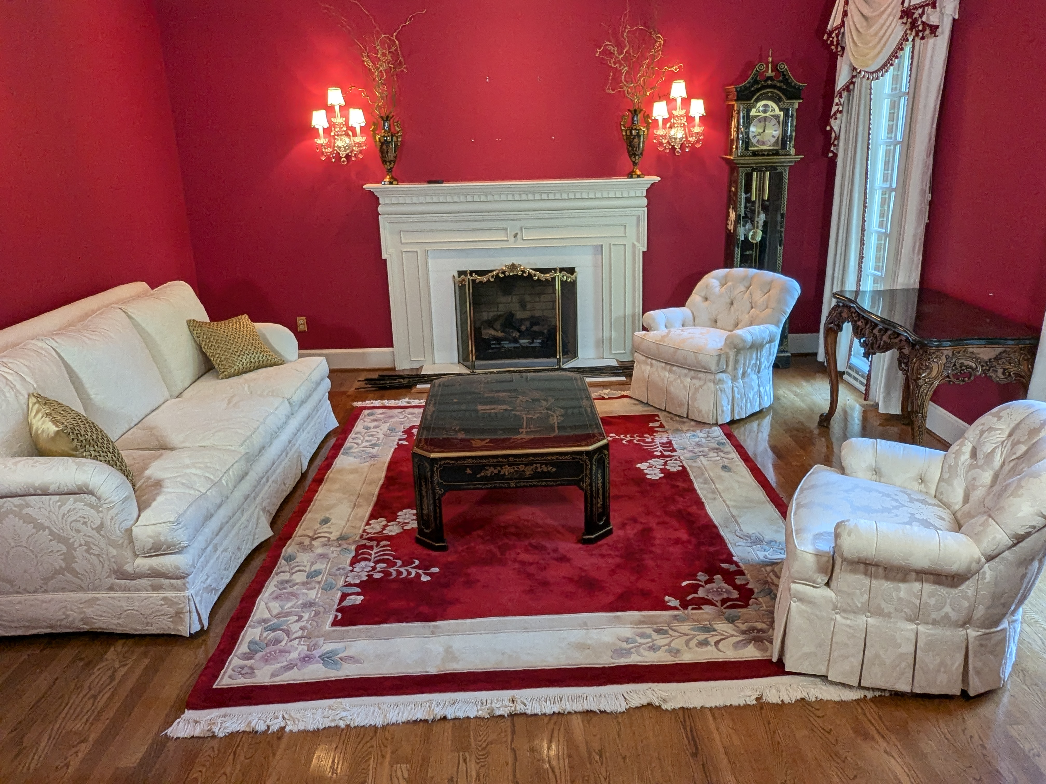 Red sitting room with a Chinese carved wool rug, fireplace and grandfather clock at the Barrington estate sale