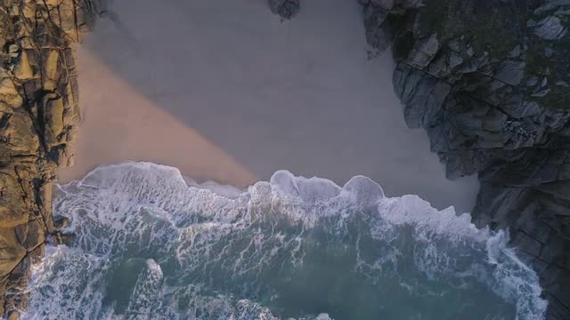Beach waves between cliffs at sunrise