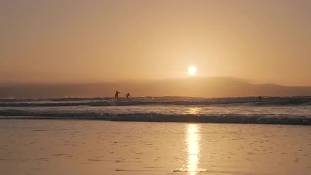 Sunset waves surfers at Gwithian Beach in Cornwal, UK