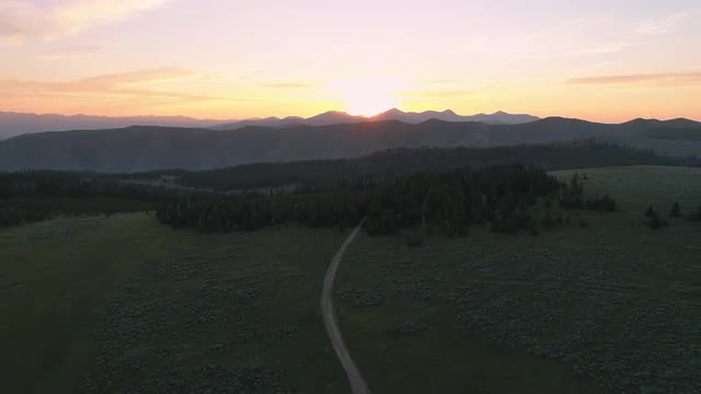 Aerial view flying high over dirt road in meadow at sunset