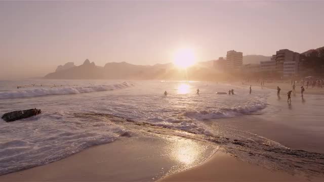 Shot of the sun about to set with people on the beach in Rio, Brazil.