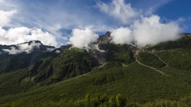 Time lapse of clouds rolling over green mountains with melting glaciers 4K