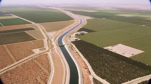 WIDE AERIAL POV over farm fields with canal running through the middle, California