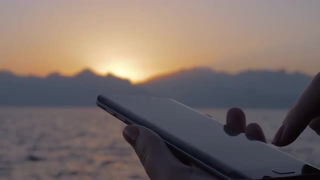 Woman using cellphone on sea and sunset background
