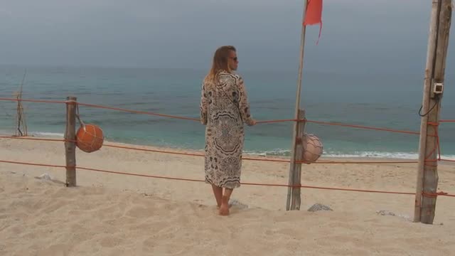 Pensive woman stands near rope fence on snady beach. Storm coming from the sea
