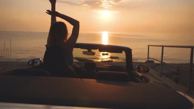 Dancing woman shakes hair. Luxury convertible car parked near sunset beach