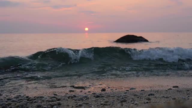 Pink sunset sky over the sea. Waves roll on sand and pebbles on a coast