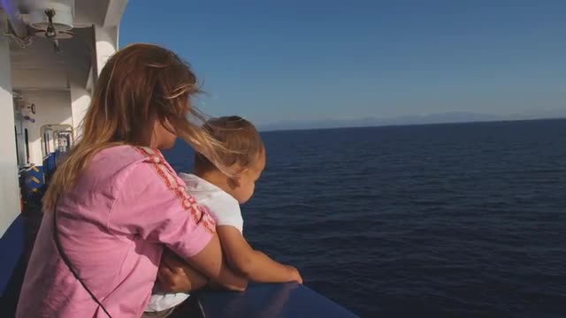 Mother with baby at the deck of ferry boat floating in blue sea. Windy sunny day