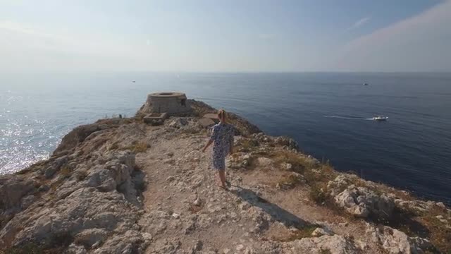 Barefoot woman walks on stony cape. Sunny day on sea coast in Italy