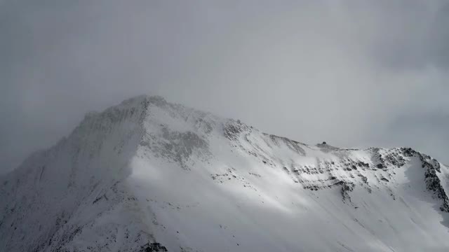 Clouds and sunlight moving across snow covered mountain peak