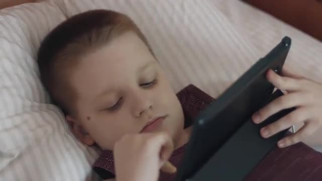 Boy Using Tablet Computer Lying In Bed