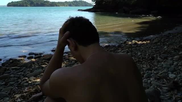 troubled young man sitting on the beach and holding his hand, loneliness, depression, opressed
