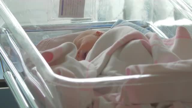 A newborn baby girl lying awake in a hospital baby cart