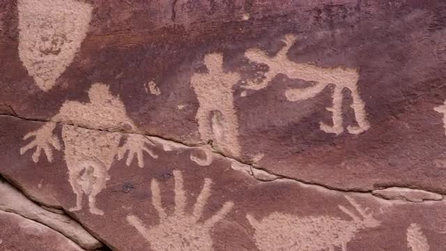 Panning over petroglyph carving of people and hands 