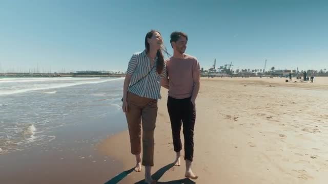 A happy couple walking down the beach barefoot holding hands