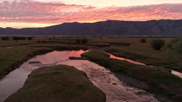 Flying over winding river at dawn as sunrise reflects in water