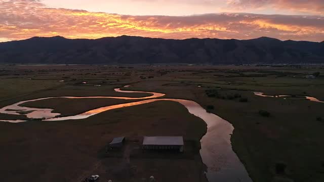 Rotating aerial view of pasture with winding river during colorful sunrise