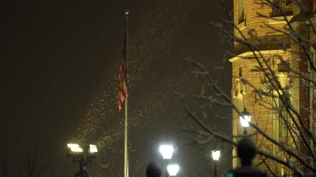 Spotlights shining on American Flag as snow falls at night in Provo