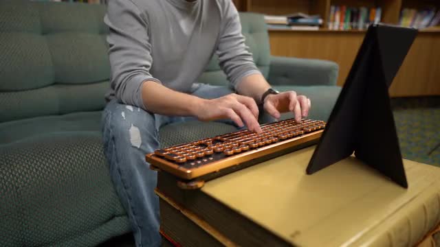 Man's hands types text with wooden keyboard and Fire HD tablet on sofa home in library