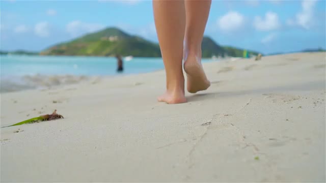 Close up female feet walking barefoot on sea shore at sunset. Slow Motion.