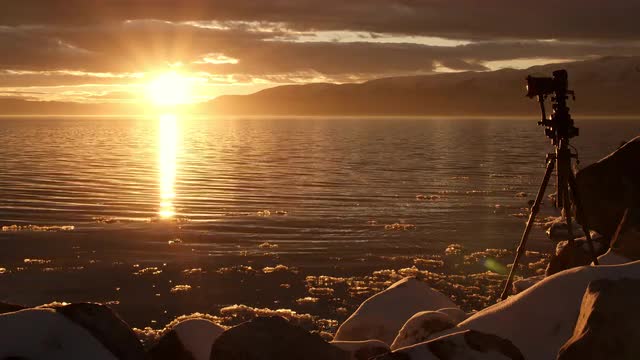 Camera at the edge of a lake during sunset reflecting in winter