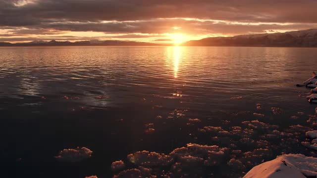 Ice floating on shoreline during golden sunset over lake
