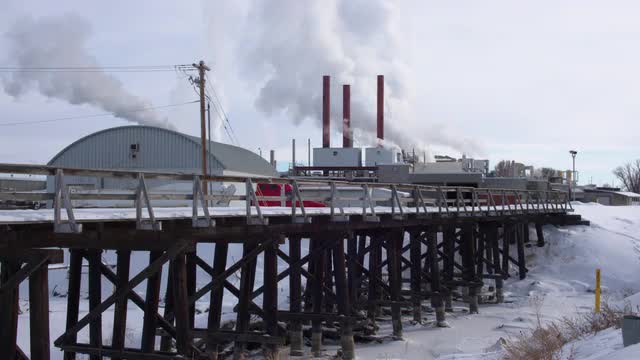Old train track bridge leading to factory as steam rises from plant