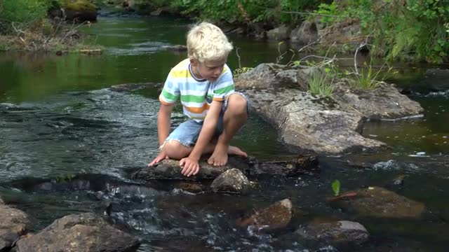 young boy playing with bark boat in small river