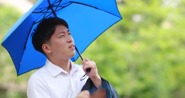 Young Japanese man repairing from the Summer sun with umbrella downtown Tokyo