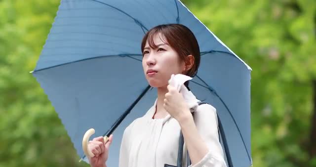 Young Japanese woman repairing from the Summer sun with umbrella downtown Tokyo
