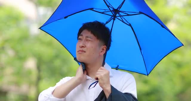 Young Japanese man repairing from the Summer sun with umbrella downtown Tokyo