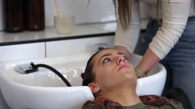Young woman rinsing another's hair in a sink at a salon